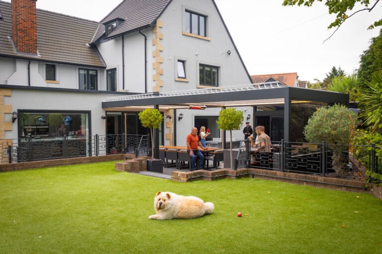 Large aluminium pergola with glazed and louvred side panels attached to a period style home, with family seating on the terrace