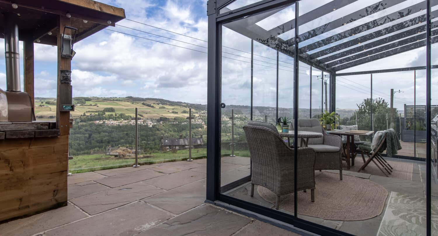 Exterior view of a glass veranda showing frameless glass sliding doors and glass balustrade