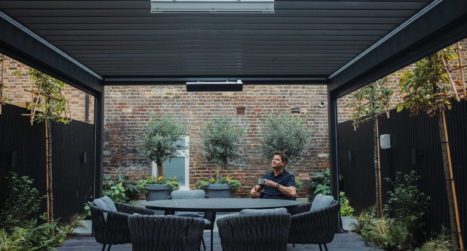 George Clarke sitting at his outdoor dining table under his bioclimatic pergola
