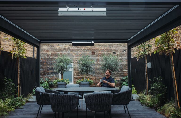 George Clarke sitting at his outdoor dining table under his bioclimatic pergola